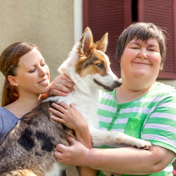 caregiver and a mentally disabled woman holding a dog smiling at the camera